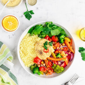 Gemüse-Bowl mit Hummus, Couscous, Babyspinat und Ofengemüse in einer weißen Schüssel von oben