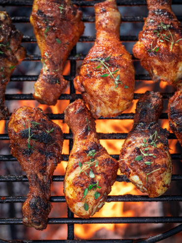 Gegrillte Hähnchenschenkel mit karamellisierter Honig-Paprika-Glasur und Thymian auf dem Grillrost