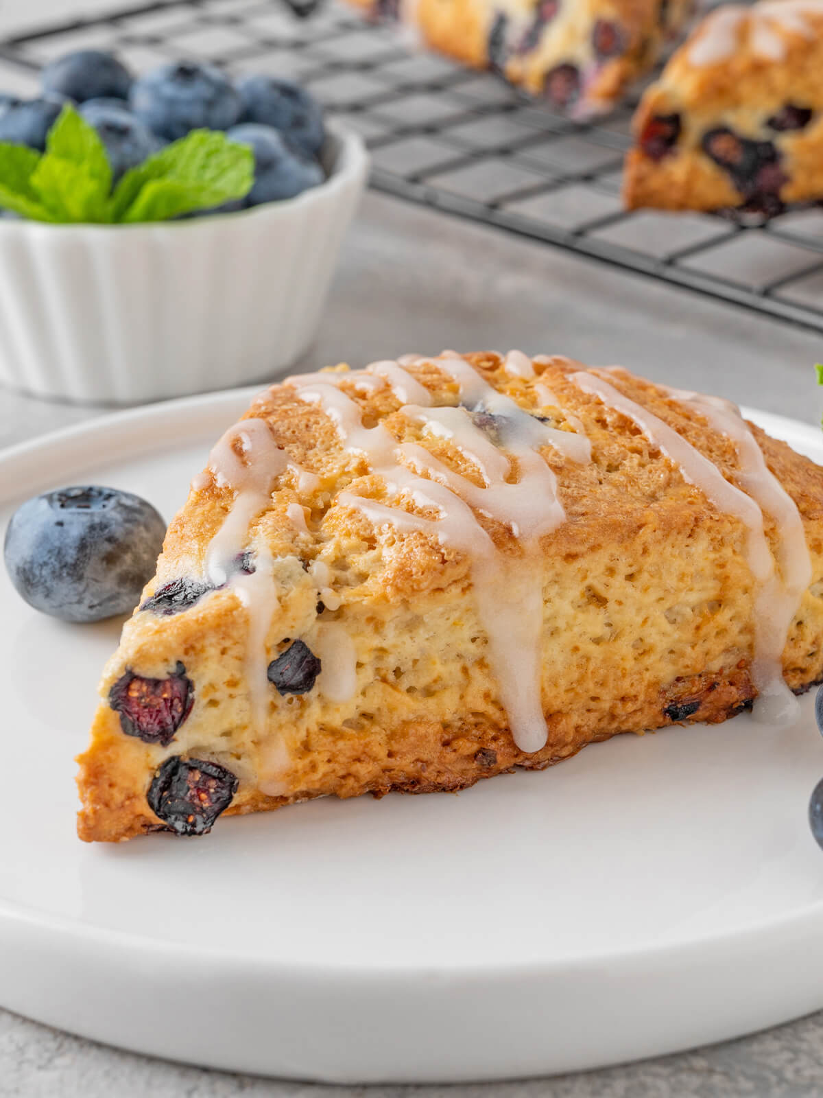 Heidelbeer-Scone mit Zitronenglasur, saftigen Blaubeeren und Minze auf weißem Teller