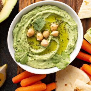 Cremiger grüner Hummus mit Avocado in Schale, dekoriert mit Olivenöl und Kichererbsen