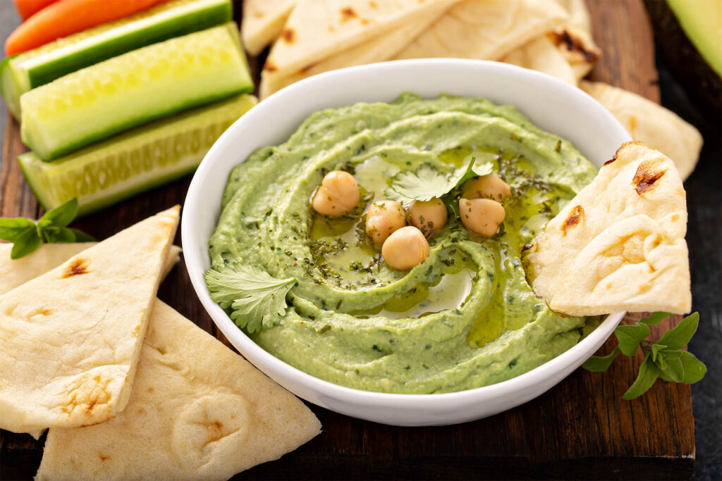 Cremiger grüner Hummus mit Avocado in Schale, dekoriert mit Olivenöl und Kichererbsen