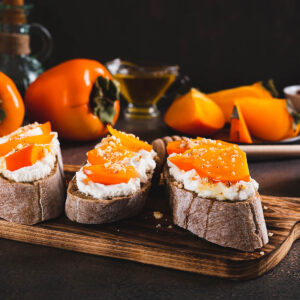 Süße Bruschetta mit Ricotta, Kaki und Honig auf Holzbrett