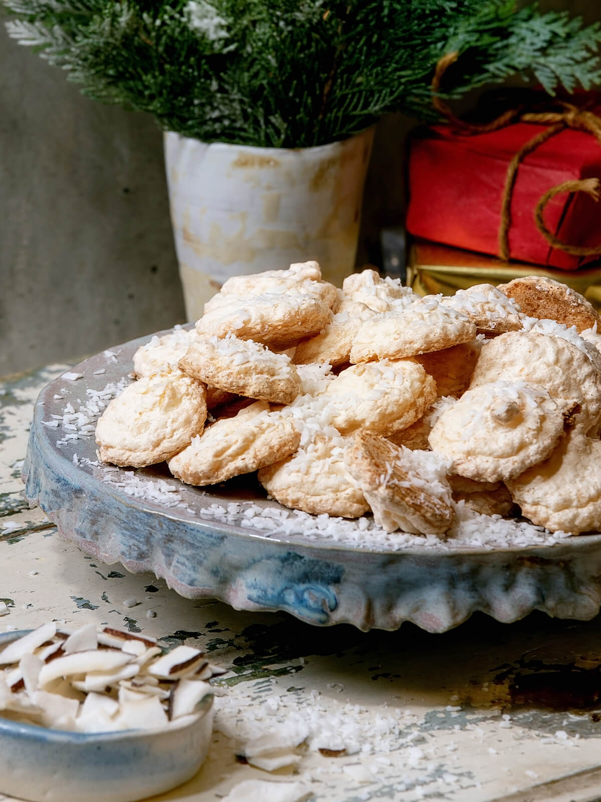 Goldgebackene Kokosmakronen mit Puderzucker auf Keramikteller, im Hintergrund Tannenzweige und festliche Geschenke