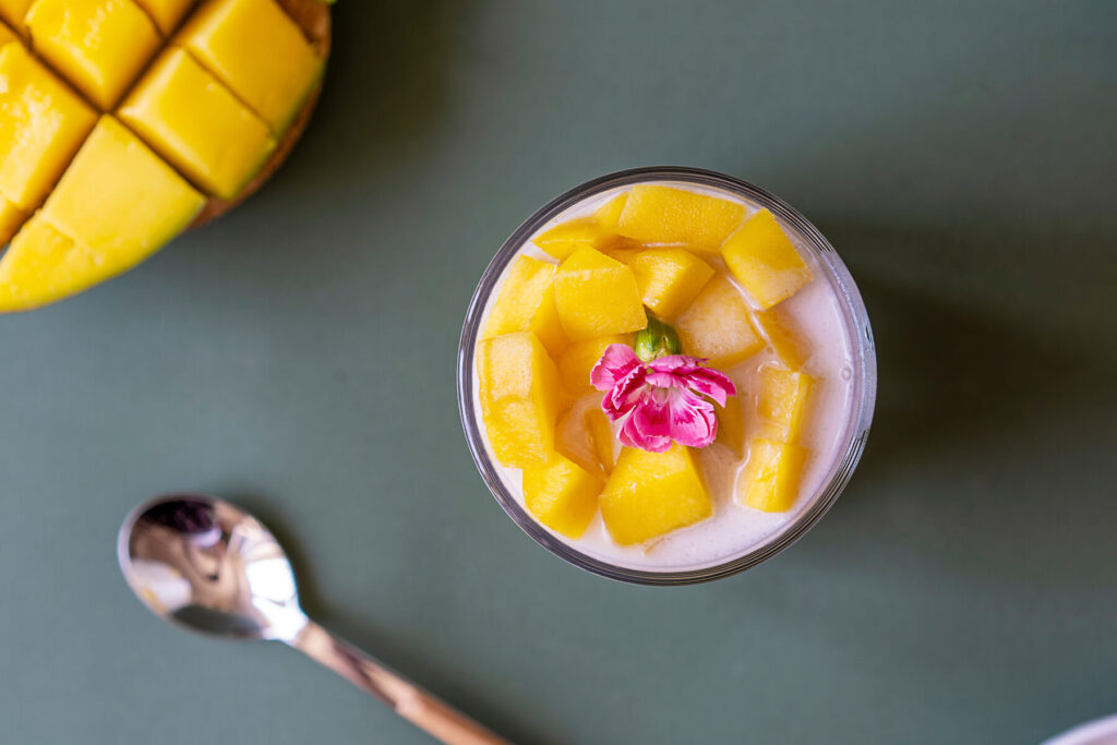 Thailändisches Mango Sticky Rice Dessert mit Klebreis, Kokosmilch und gewürfelter Mango im Glas mit Edelblüte