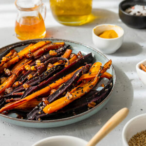 Marokkanische glasierte orange und violette Karotten auf Keramikteller mit Honig und Gewürzen