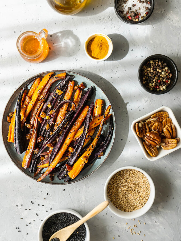 Marokkanische glasierte orange und violette Karotten mit Honig-Glasur, Pekannüssen und Sesam in dunkler Keramikschale