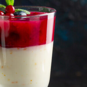 Zweischichtiger Milchpudding mit Preiselbeeren im Glas, weiße Schicht unten, rote Beerenschicht oben