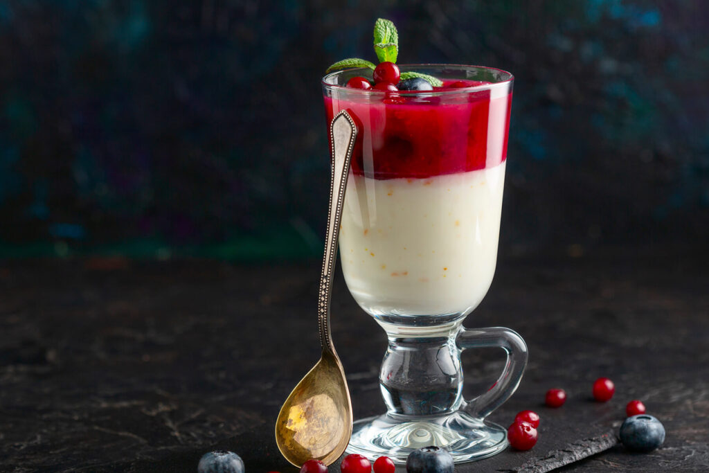 Fertiges Glas mit Milchpudding und Preiselbeer-Schicht, garniert mit frischen Beeren und Minze