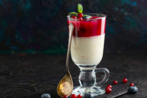 Fertiges Glas mit Milchpudding und Preiselbeer-Schicht, garniert mit frischen Beeren und Minze