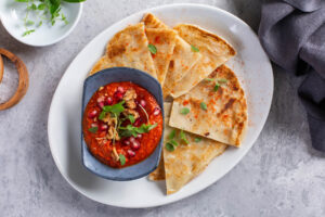 Syrische Muhammara mit Granatapfelkernen, gehackten Walnüssen und frischem Oregano in blauer Keramikschale, dazu pfannengeröstetes Fladenbrot