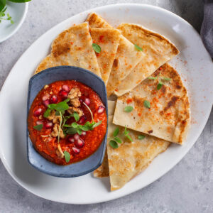 Syrische Muhammara mit Granatapfelkernen, gehackten Walnüssen und frischem Oregano in blauer Keramikschale, dazu pfannengeröstetes Fladenbrot