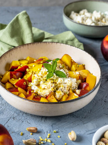 Nektarinen-Ricotta-Salat in heller Keramikschale mit gelb-roten Fruchtwürfeln, Ricotta-Mascarpone-Creme und gehackten Pistazien