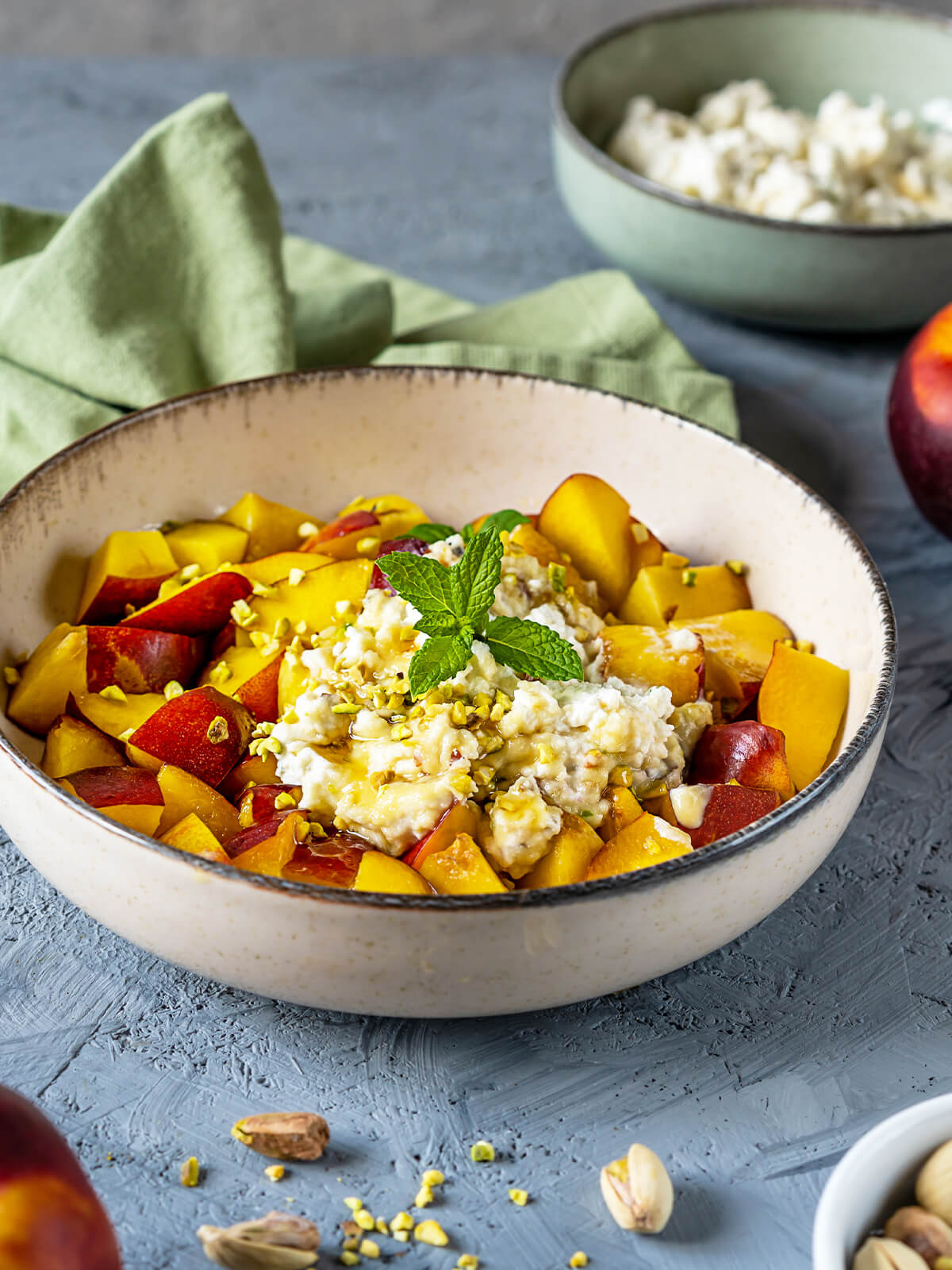 Nektarinen-Ricotta-Salat in heller Keramikschale mit gelb-roten Fruchtwürfeln, Ricotta-Mascarpone-Creme und gehackten Pistazien