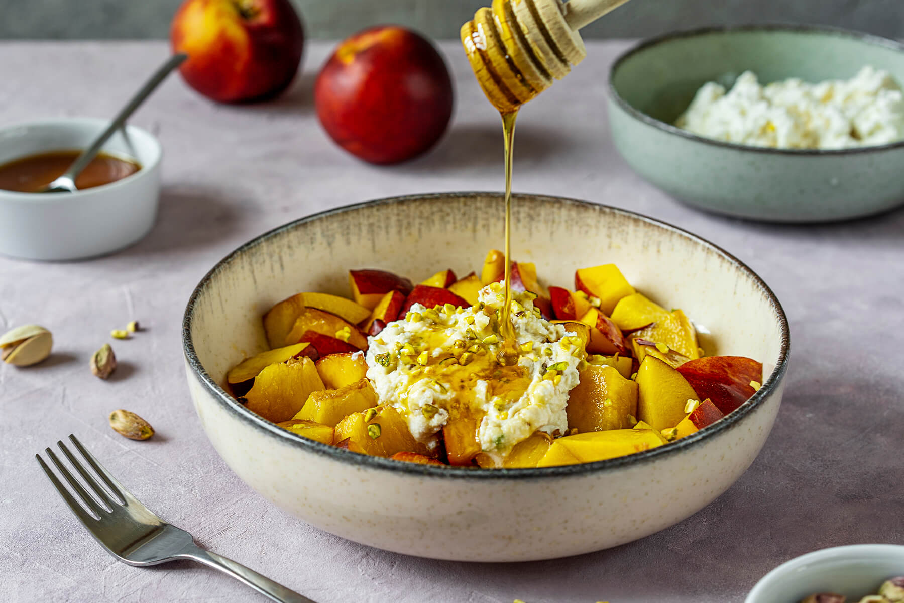 Honig wird mit einem Holzlöffel über Nektarinen-Ricotta-Salat mit Pistazien geträufelt