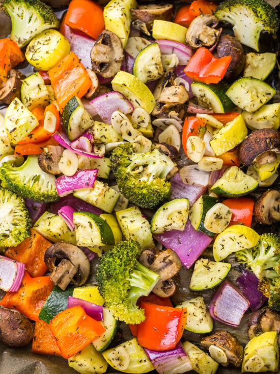 Buntes Ofengemüse mit halbierter roter Bete, Karotten und Champignons auf einem dunklen Teller, daneben eine Schale Hummus