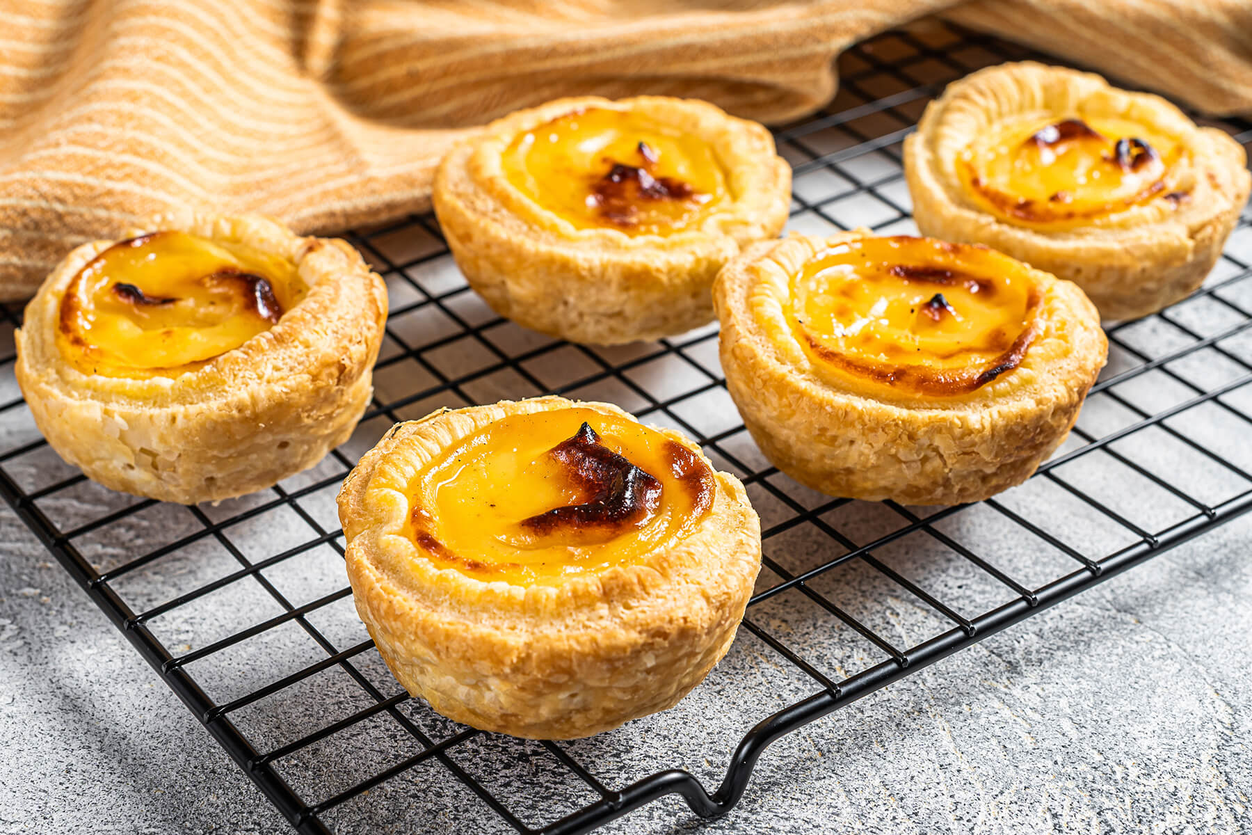 Fünf Pastéis de Nata mit sichtbaren Blätterteigschichten an der Außenwand auf einem Abkühlgitter