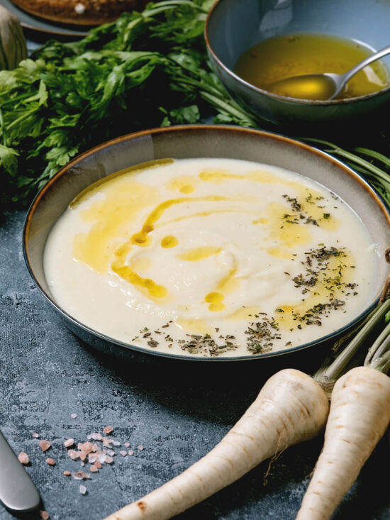 Cremige Pastinaken-Suppe in dunkler Schale mit brauner Butter, Pastinaken-Chips und frischen Kräutern