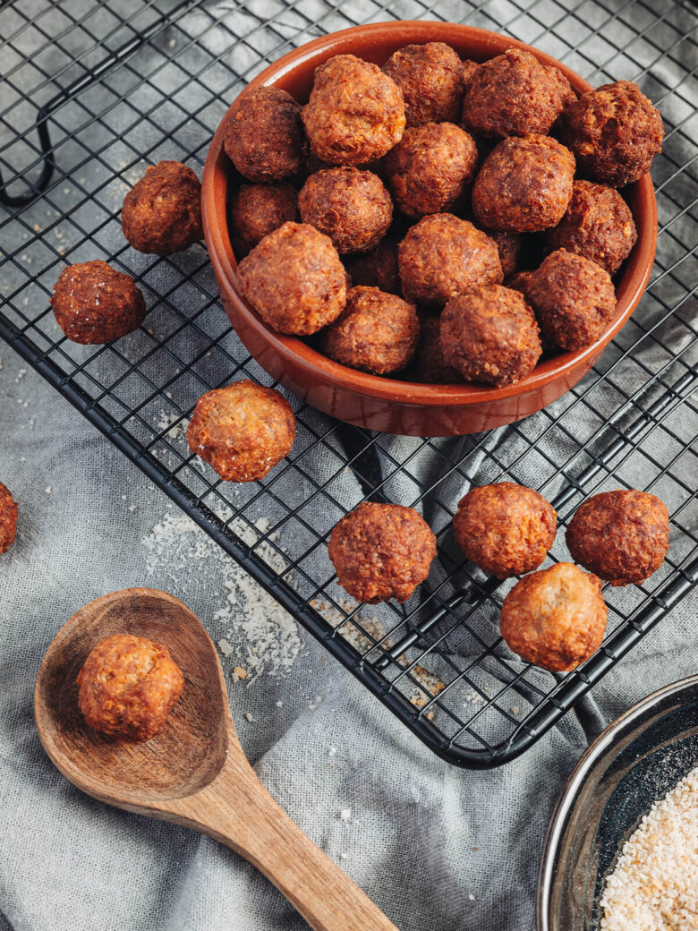 Goldbraune frittierte Polpette al Parmigiano in terracotta-farbener Schale auf Kühlrost als italienisches Antipasto