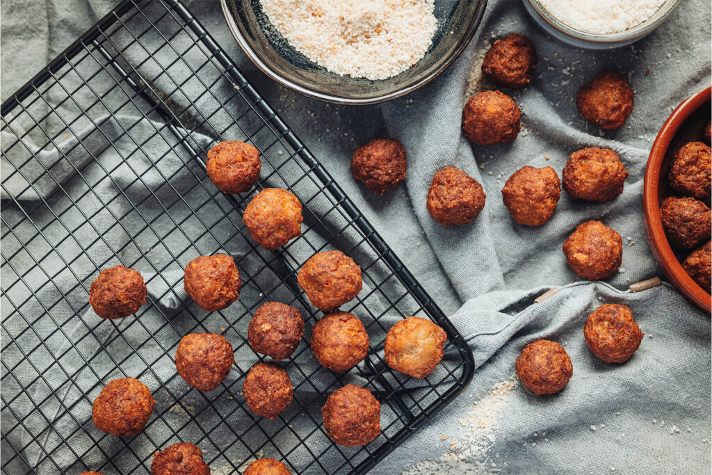 Goldbraune frittierte Polpette al Parmigiano in einer terracotta-farbenen Schale auf schwarzem Kühlrost, italienisches Antipasto