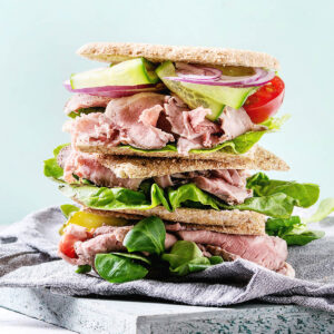 Hoch gestapeltes Roastbeef-Sandwich mit rosa Roastbeef, Salat, Gurke, Zwiebel und Tomate