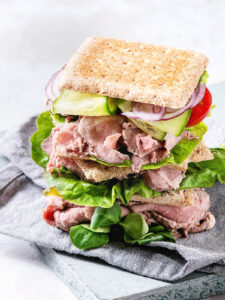 Gestapeltes Roastbeef-Sandwich mit dünn geschnittenem Roastbeef, frischen Salatblättern, Gurke, roten Zwiebelringen und Kirschtomaten in Vollkorn-Pita