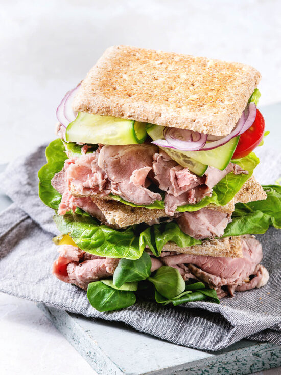 Gestapeltes Roastbeef-Sandwich mit dünn geschnittenem Roastbeef, frischen Salatblättern, Gurke, roten Zwiebelringen und Kirschtomaten in Vollkorn-Pita