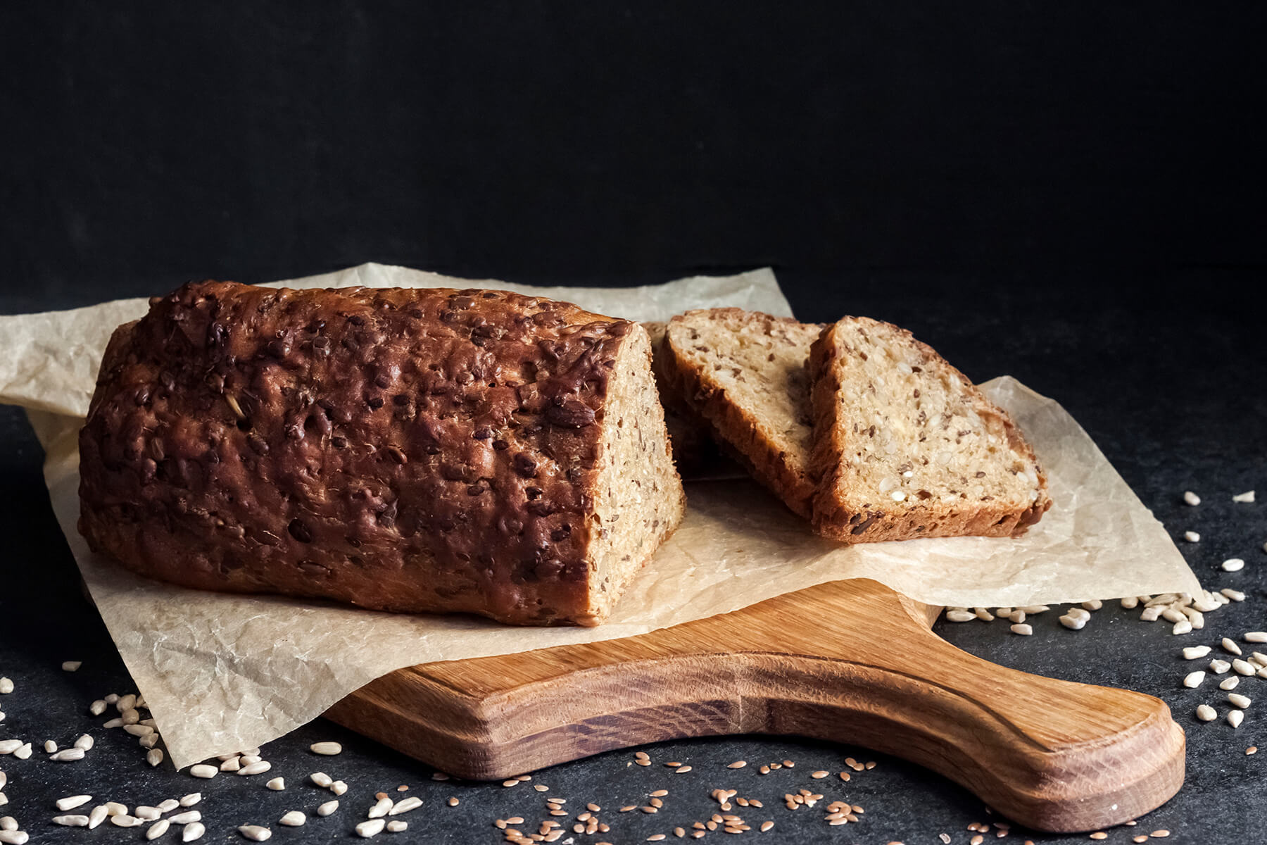 Ganzes Saaten-Brot mit dunkel glänzender Oberseite auf Backpapier