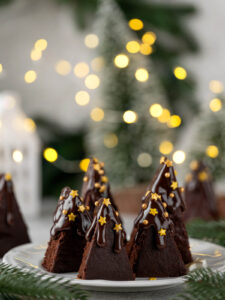 Verzierte Brownie-Tannenbäume mit goldenen Zucker-Sternen und goldenen Zuckerperlen vor Lichterkette
