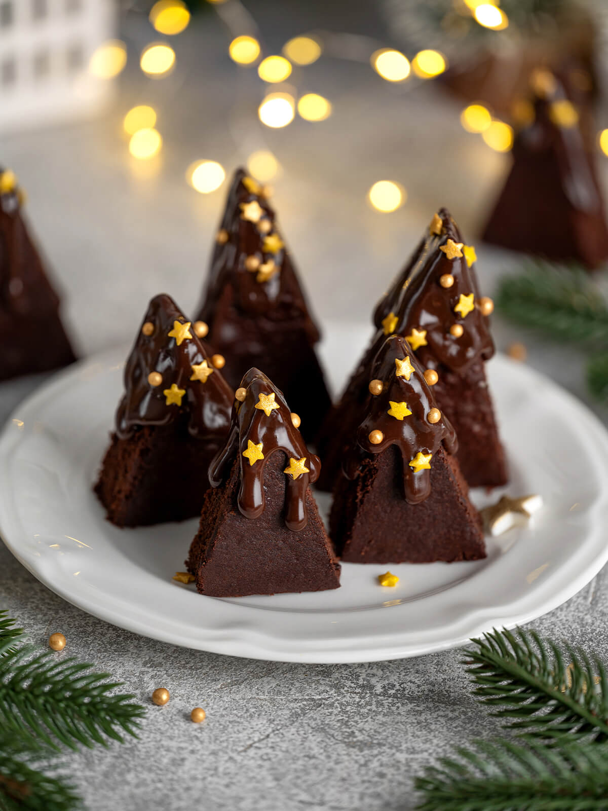 Schoko-Brownie-Tannenbäume mit Schokoglasur, goldenen Sternen und goldenen Zuckerperlen auf weißem Teller