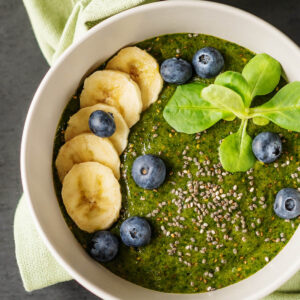 Grüner Smoothie Bowl in einer Schüssel, getoppt mit Banane, Heidelbeeren, Chiasamen und Feldsalat