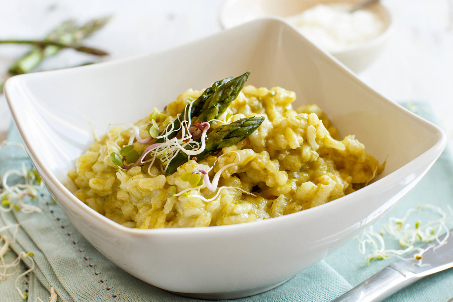Cremiges Spargel-Risotto mit Parmesan und Taleggio in einer weißen Schale, garniert mit ganzen Spargelspitzen und Sprossen