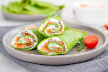 Angeschnittene grüne Crêpe-Röllchen mit Lachs und Frischkäse auf einem grauen Teller