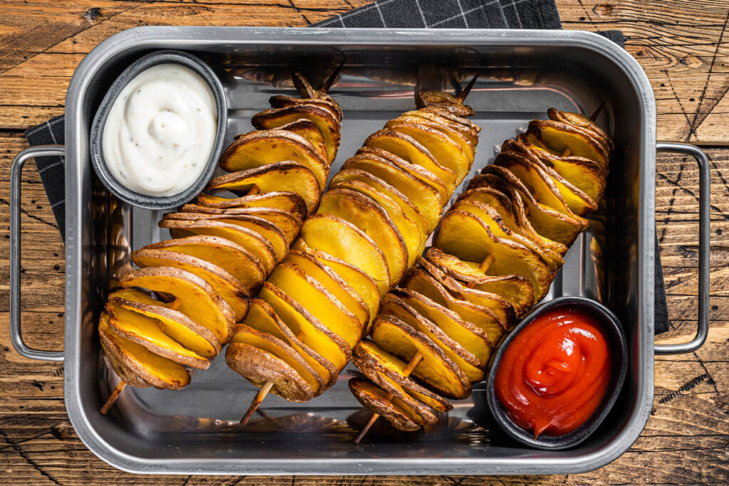Tornado-Kartoffeln am Spieß aus dem Ofen mit Ketchup und hellem Knoblauch-Dip in einer Edelstahlschale