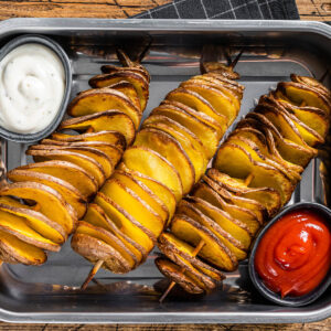 Tornado-Kartoffeln am Spieß aus dem Ofen mit Ketchup und hellem Knoblauch-Dip in einer Edelstahlschale