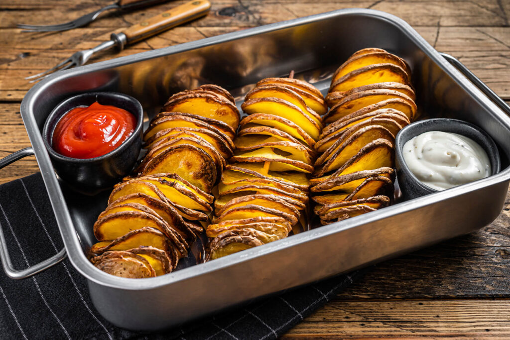 Gebackene Tornado-Kartoffeln am Holzspieß in einer Edelstahlschale mit Ketchup und Knoblauch-Kräuter-Dip