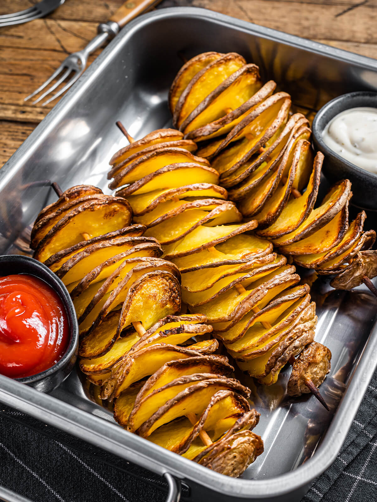 Tornado-Kartoffeln am Spieß aus dem Ofen mit dunkelbraunen Schalenrändern, daneben Ketchup und heller Knoblauch-Dip