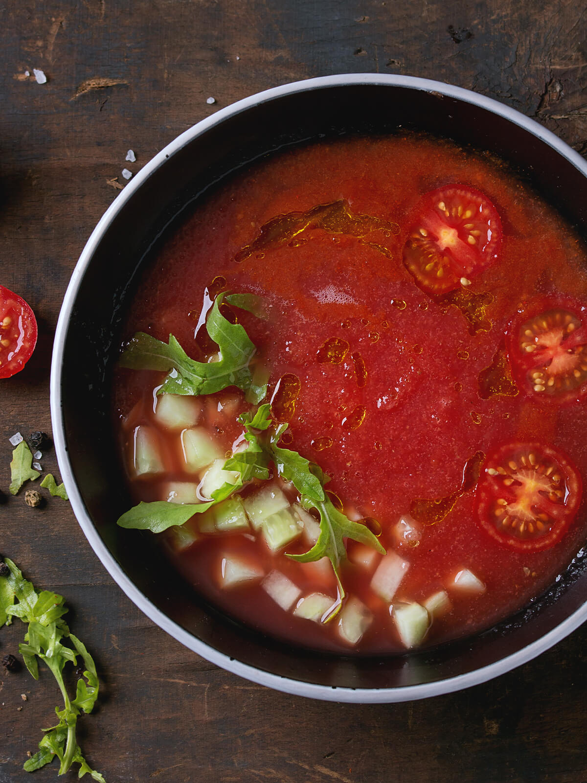 Wassermelonen-Gazpacho in dunkler Schale mit Gurken-Würfeln, Rucola und Olivenöl von oben fotografiert