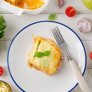 Stück Zucchini-Lasagne auf einem Teller mit blauem Rand, garniert mit frischem Basilikum