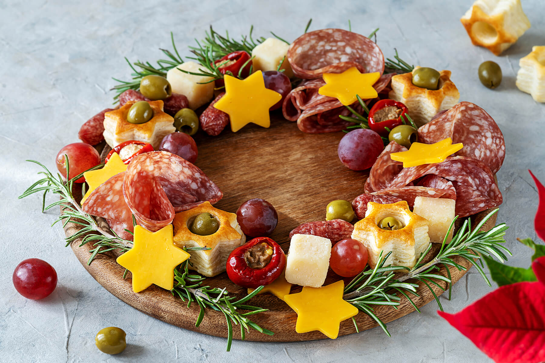 Nahaufnahme des Kranzes mit goldbraunen Blätterteig-Sternen mit grüner Olive in der Mitte, orangen Käse-Sternen und gefüllter roter Mini-Paprika
