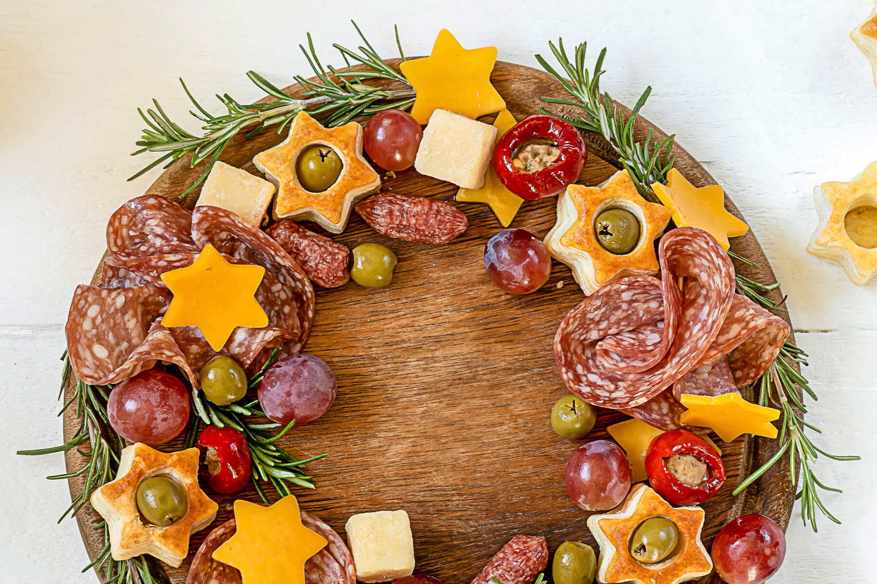 Antipasti-Kranz von oben mit Blätterteig-Sternen, Käse-Sternen, gefüllten Paprika, Salami-Röschen und Trauben rund um eine freie Mitte