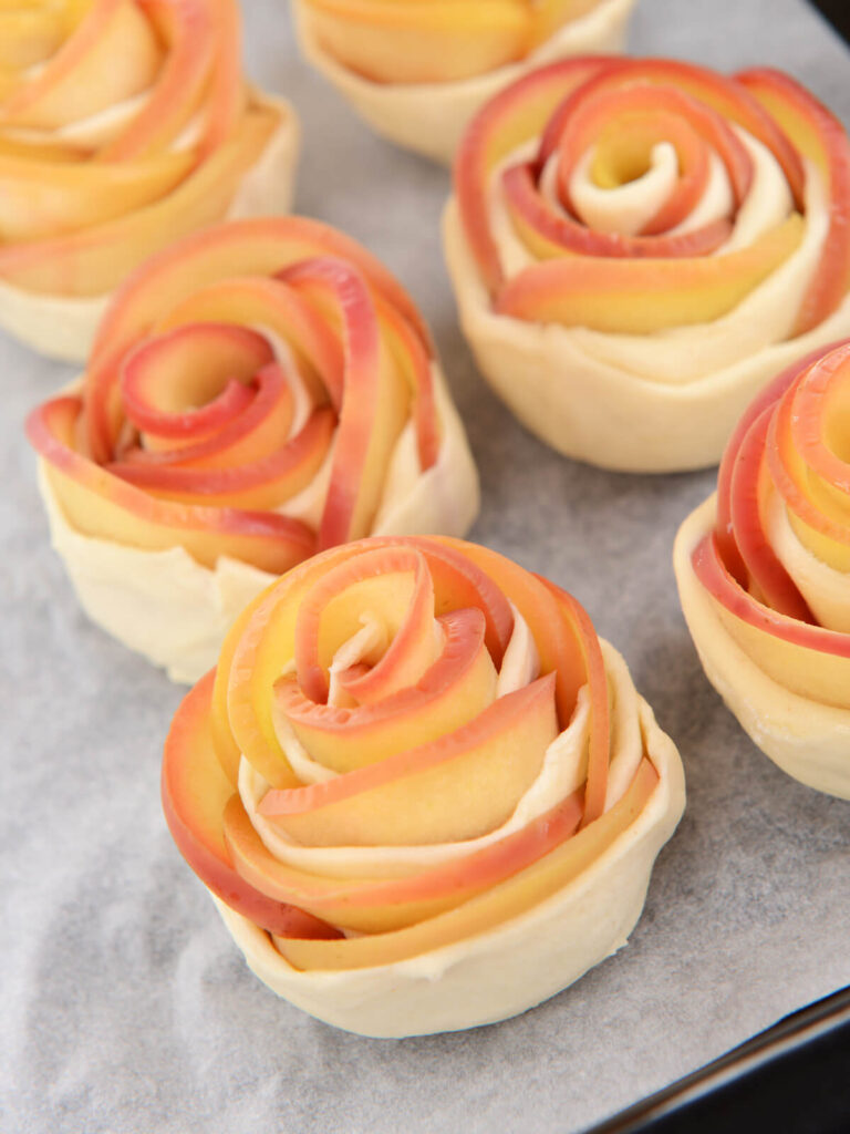 Rohe, aufgerollte Apfel-Rosen aus Blätterteig mit rot-gelben Apfelscheiben vor dem Backen