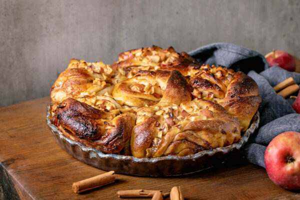 Apfel-Zimt-Pull-Apart-Brot in einer dunklen Keramikform auf einem Holzbrett