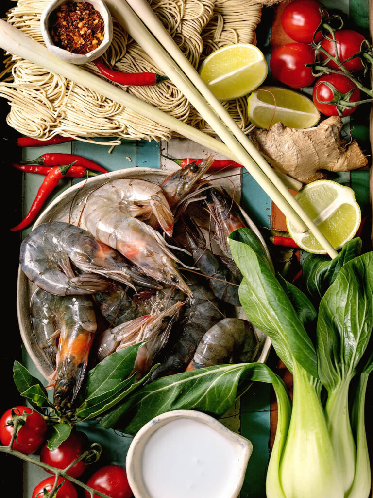 Zutaten für Asia-Nudelsuppe mit rohen Tigergarnelen in der Schale, Eiernudeln, frischem Ingwer, roten Chilis, Cherrytomaten und Limette