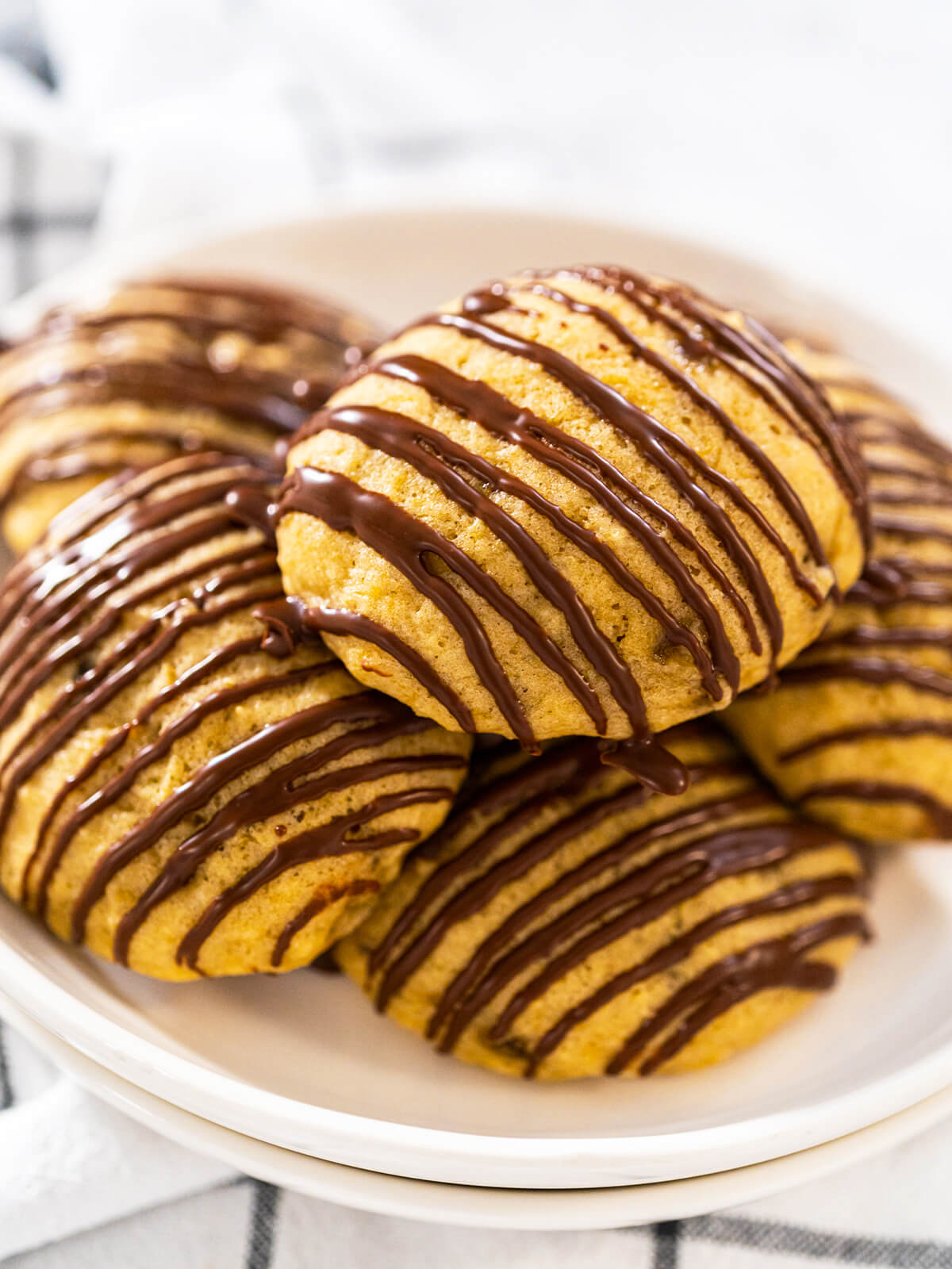 Stapel weicher Bananen-Cookies mit Schoko-Drizzle auf einem weißen Teller