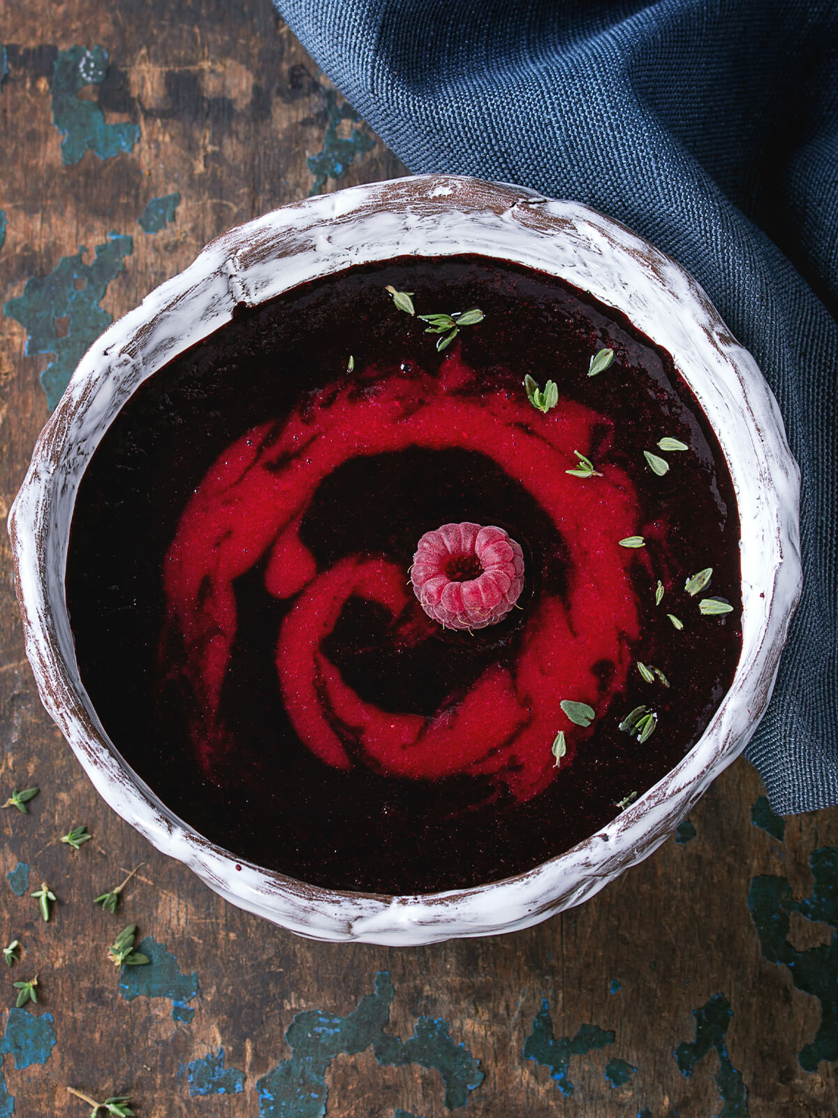 "Tief-violette Beeren-Dessert-Suppe mit rotem Himbeer-Coulis-Swirl und einer ganzen Himbeere in weiß-glasierter Keramikschale"