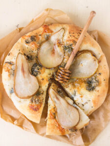 Birne-Gorgonzola-Pizza mit Honig, in Spalten geschnitten, mit Honiglöffel