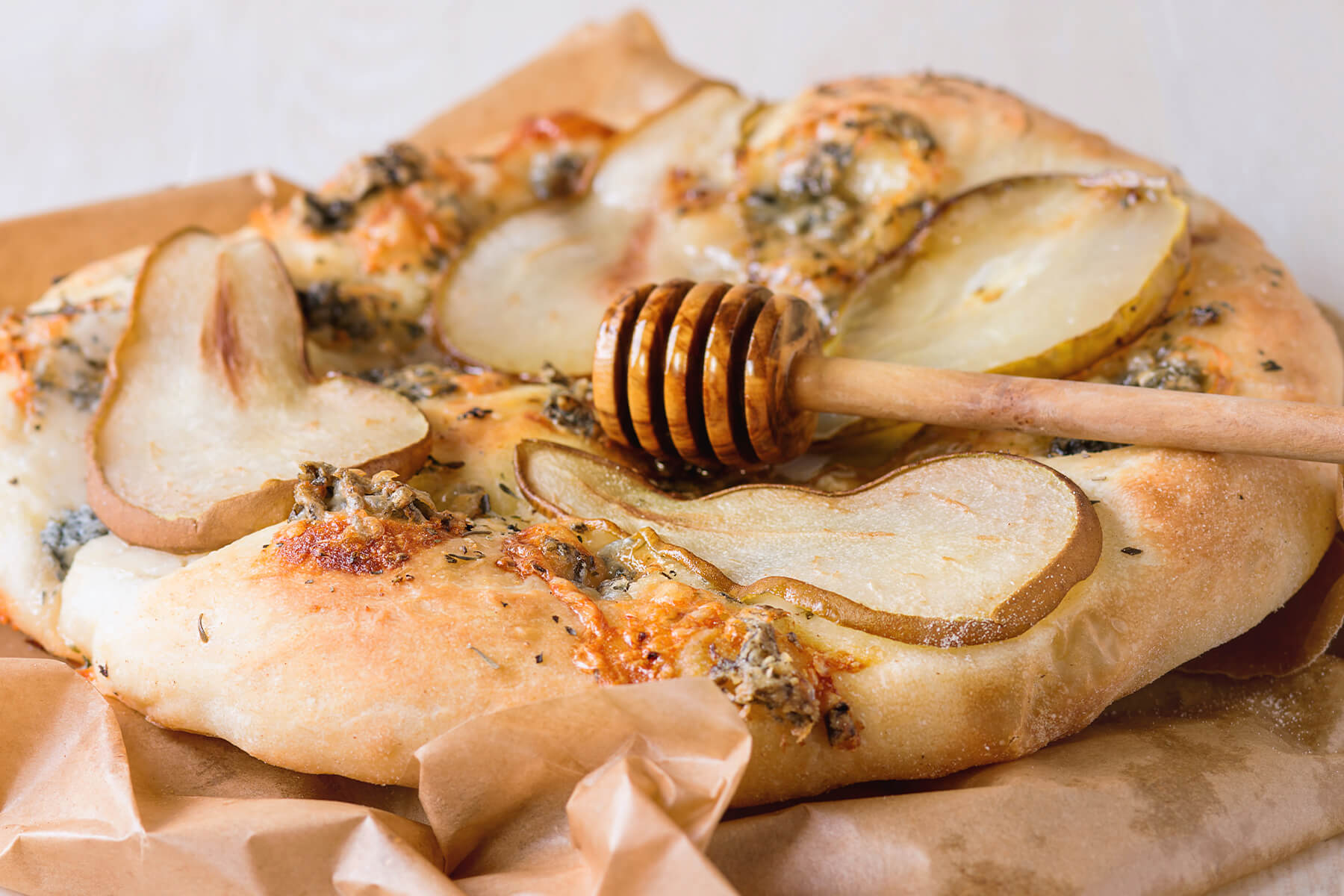 Rustikale Birne-Gorgonzola-Pizza mit Honig, ein Stück angeschnitten, Honiglöffel obenauf