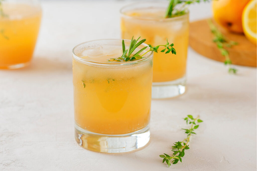 Zwei Gläser eiskalte, leicht sprudelnde Birnen-Limonade mit Kräuter-Garnitur und Eiswürfeln