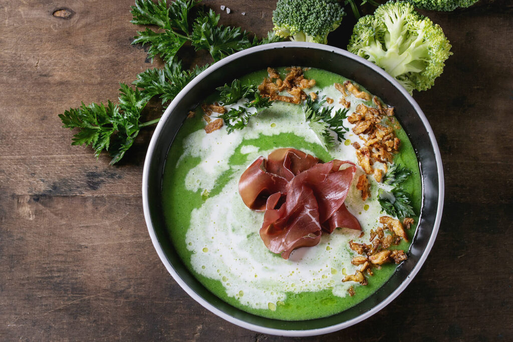 Brokkoli-Cremesuppe mit Serrano-Schinken-Rose, Sahne-Welle und knusprigen Zwiebel-Nestern