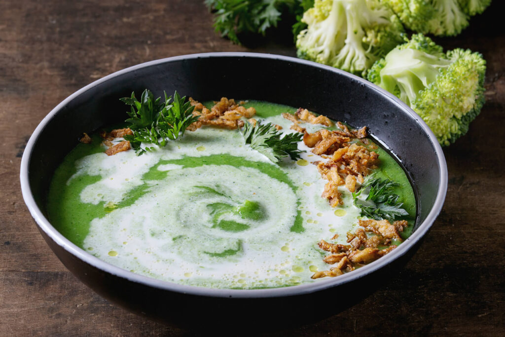 Brokkoli-Cremesuppe in dunkler Schale mit Sahne-Spirale, knusprigen Zwiebel-Nestern und Petersilie